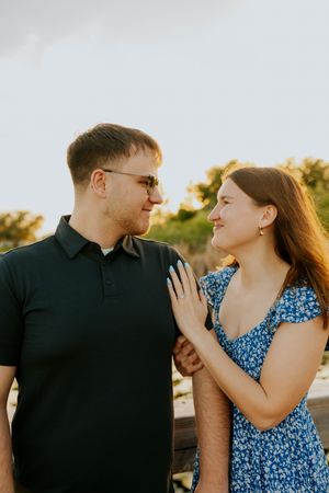 An engaged couple smiles warmly at each other during a glowing sunset portrait session outdoors.