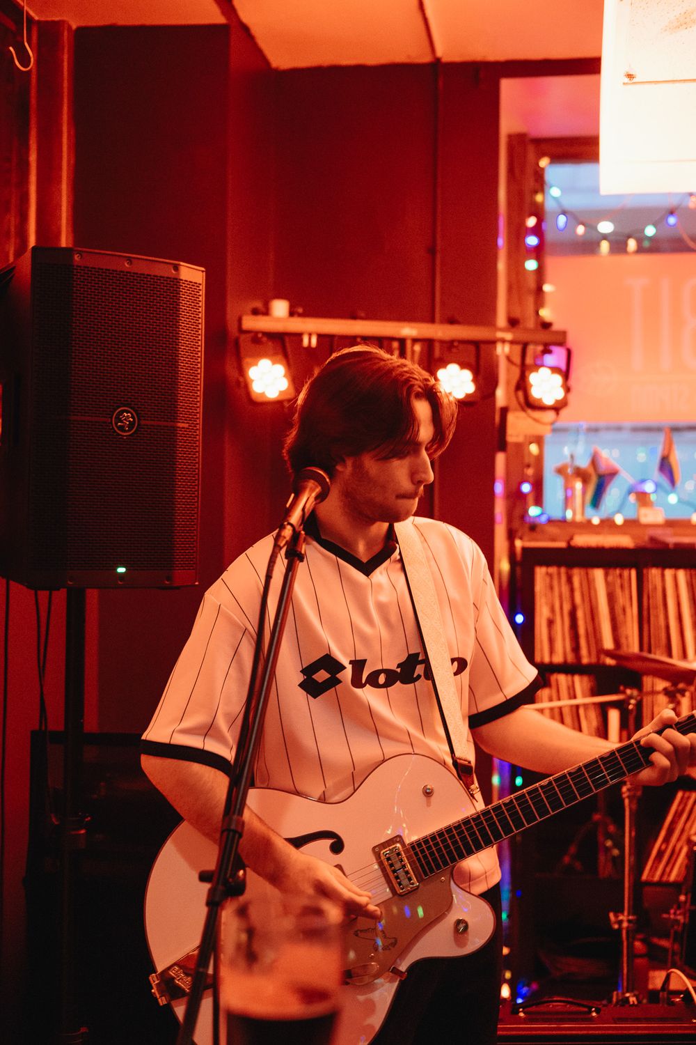 Young guitarist in white Lotto jersey playing a white hollow-body electric guitar on stage.