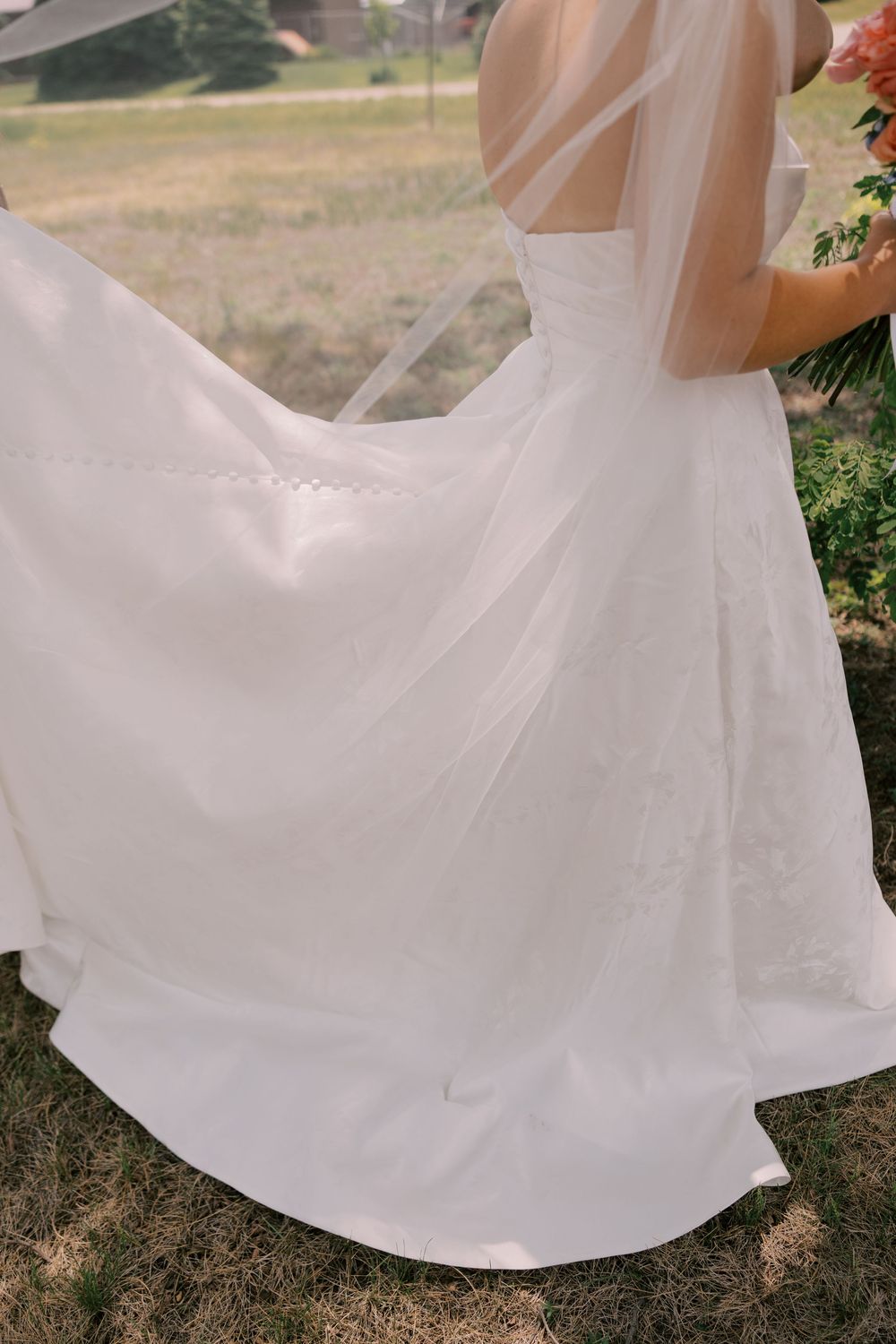 Bride in flowing white wedding gown with veil outdoors, dress billowing gracefully in the breeze.