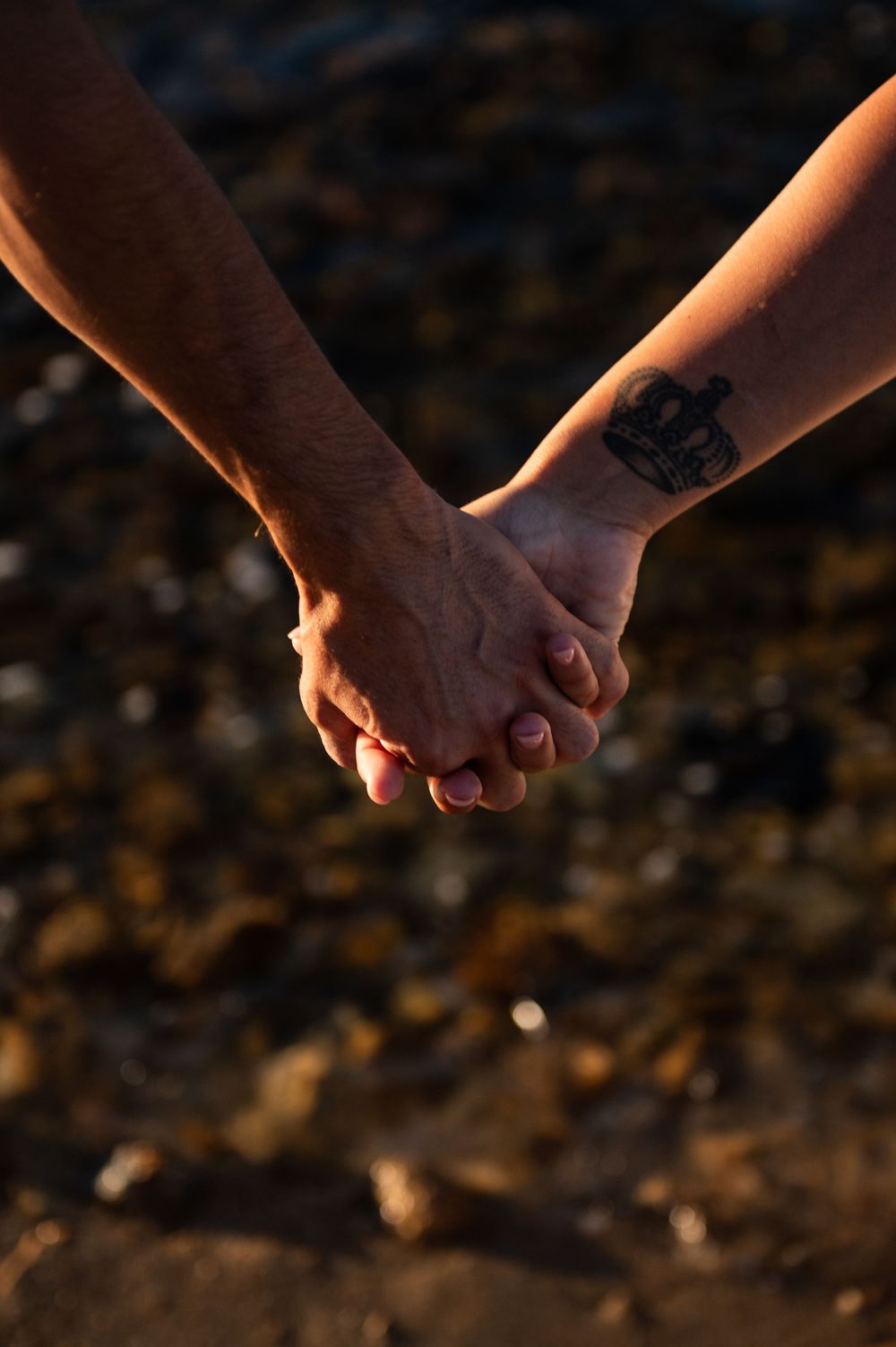 Close-up of holding hands with sunset light on a rocky beach.