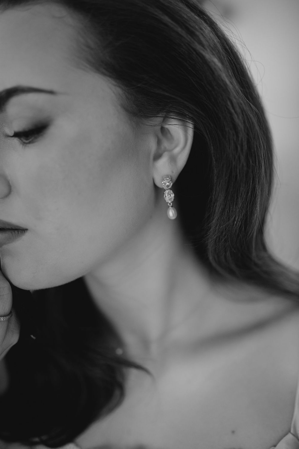 Black and white close-up of a bride wearing elegant pearl drop earrings with eyes closed.