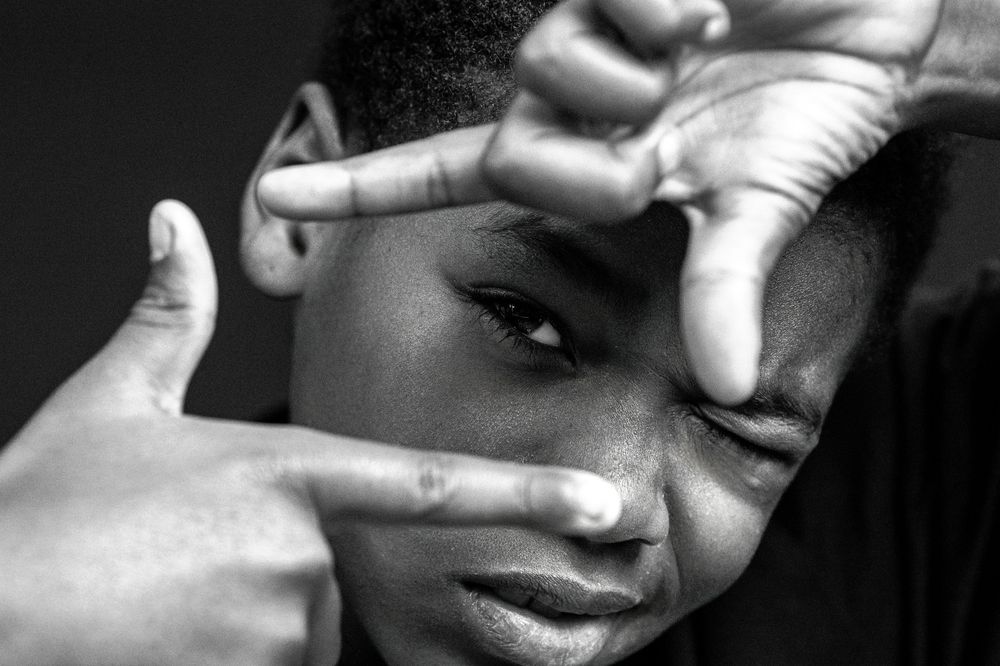 Black and white portrait of a young man framing his eye with fingers in a creative photography pose.