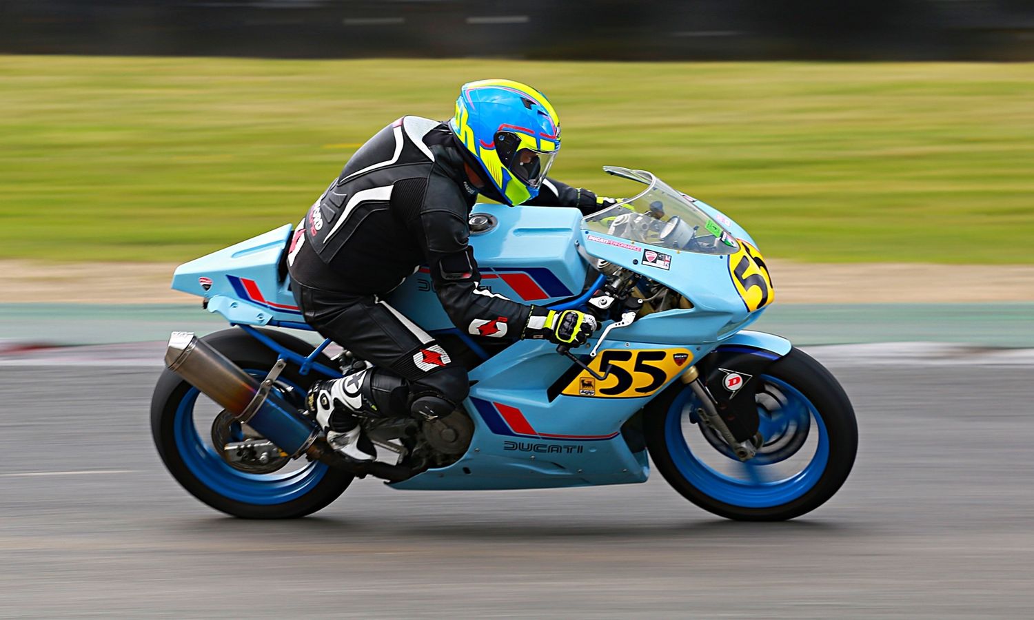 Rider number 55 on a light blue motorcycle leaning into a corner at a competitive motorsport event.