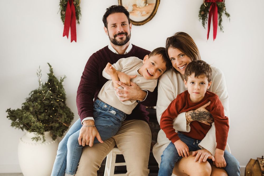 Family of four poses for a festive Christmas portrait with holiday wreaths and greenery decorations in the background.