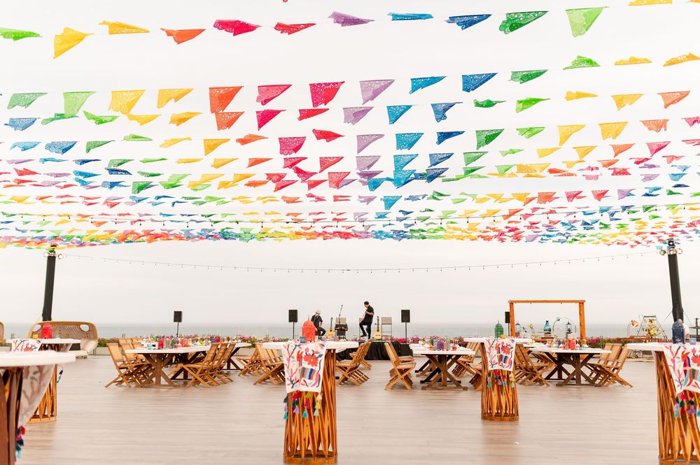 Colorful rainbow triangle bunting flags hang over wooden tables at a festive outdoor wedding reception.