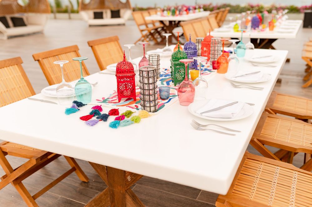 Colorful Moroccan lanterns and vibrant glassware decorate a white outdoor dining table with wooden chairs.