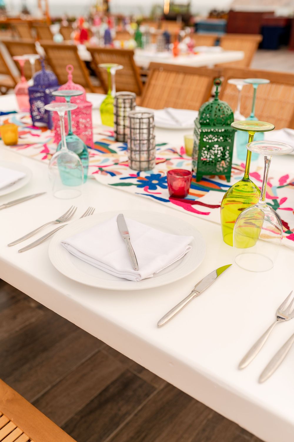 Colorful table setting with vibrant lanterns, wine glasses, and floral runner on a white tablecloth.