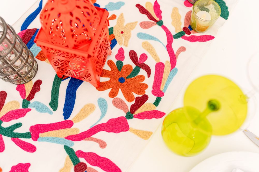 Colorful embroidered floral tablecloth with red lantern, green cocktails, and vibrant Mexican-inspired decor.
