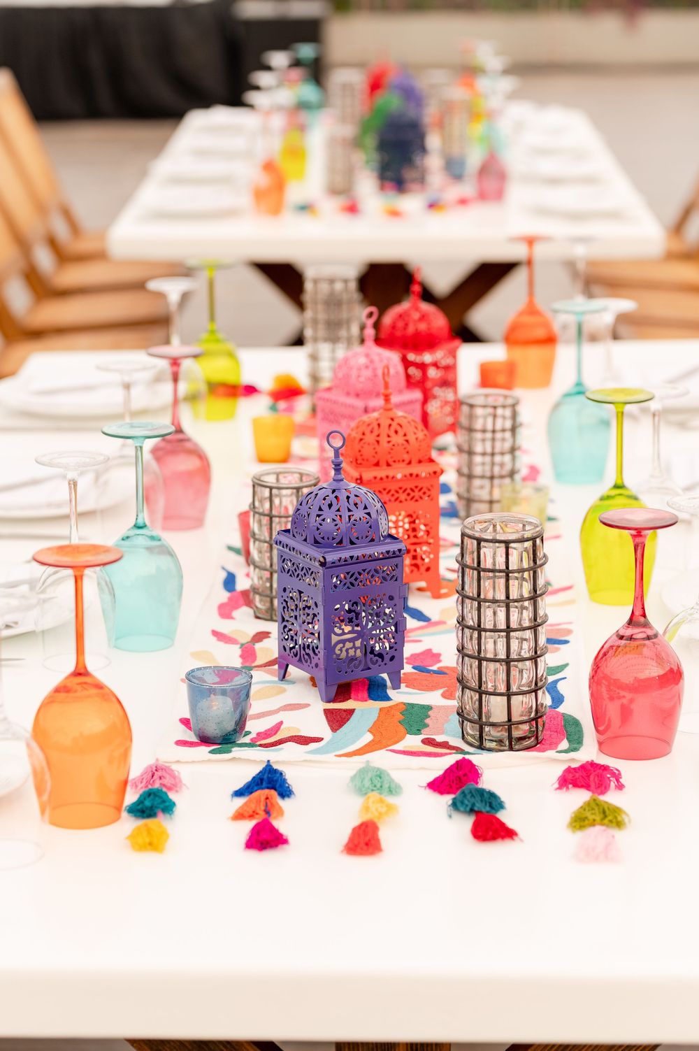 Colorful Moroccan lanterns, upside-down wine glasses, and tassels decorate a vibrant fiesta-themed wedding table setting.