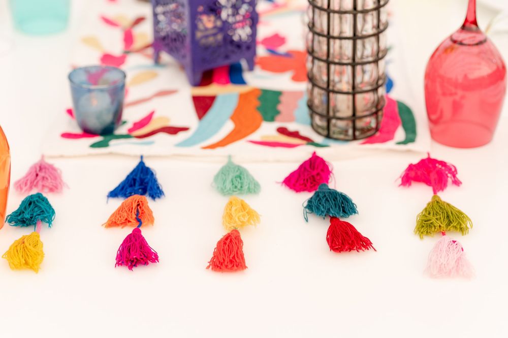 Colorful tassel garland with rainbow yarn tassels displayed on a white surface with festive party decorations.
