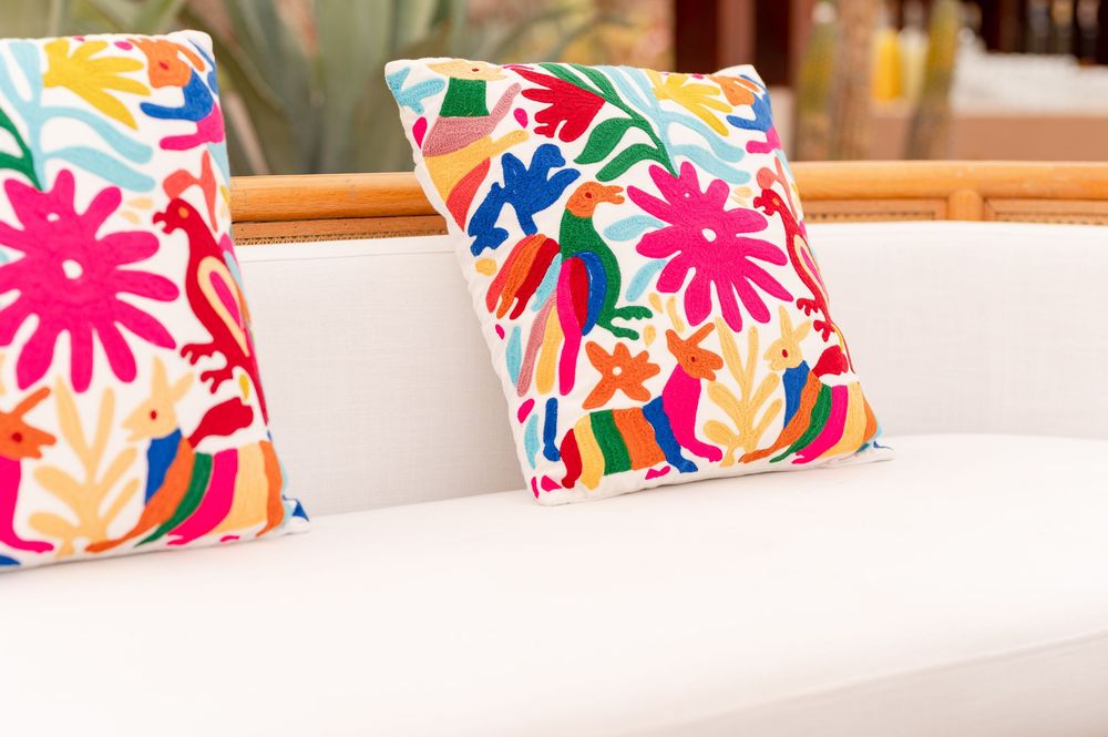 Colorful embroidered Otomi throw pillows with floral and animal patterns on a white sofa.