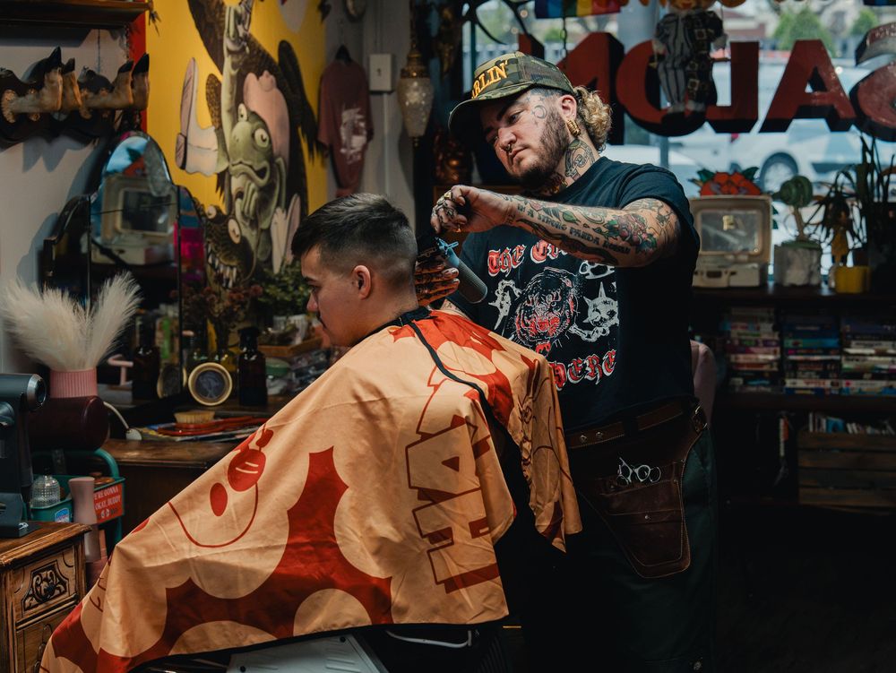 Tattooed barber cutting a client's hair in a vibrant, eclectic barbershop filled with colorful decor.