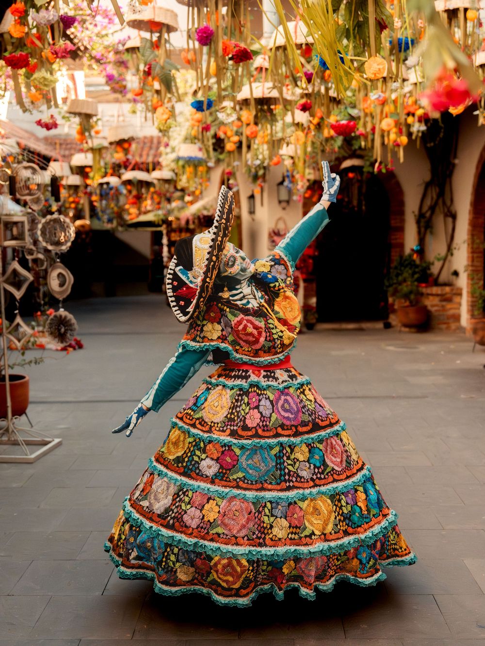 Colorful Catrina skeleton figure in embroidered dress dancing at a vibrant Mexican market with festive decorations.