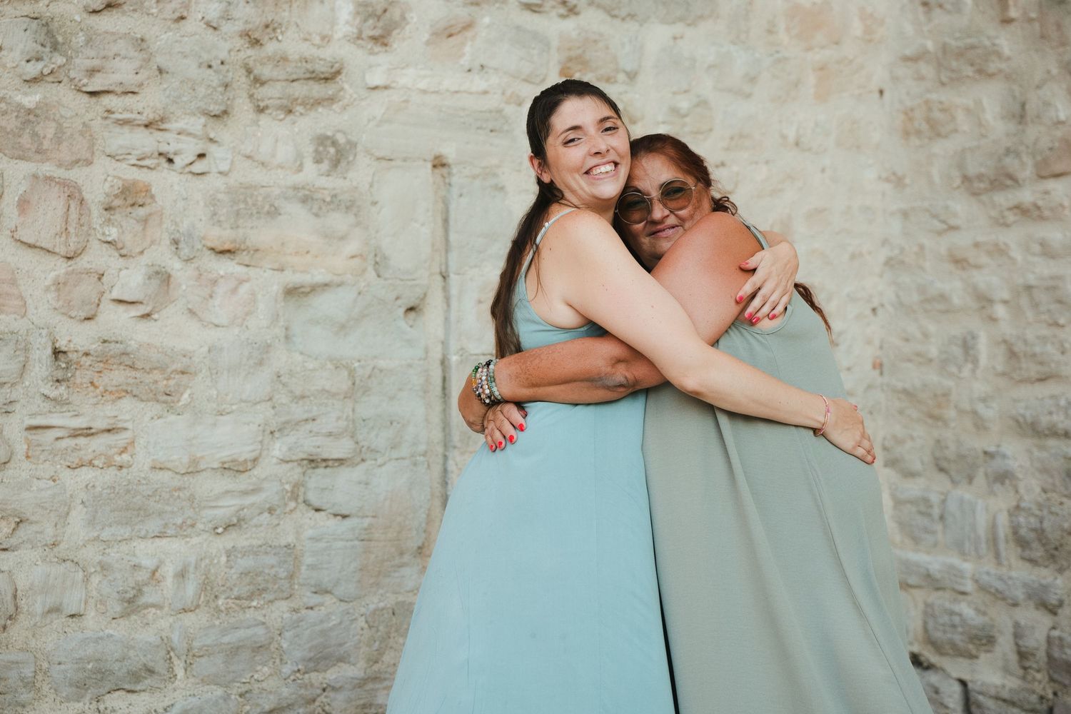 Une mère et sa fille adulte s’enlacent en souriant devant les pierres des remparts de Trets.