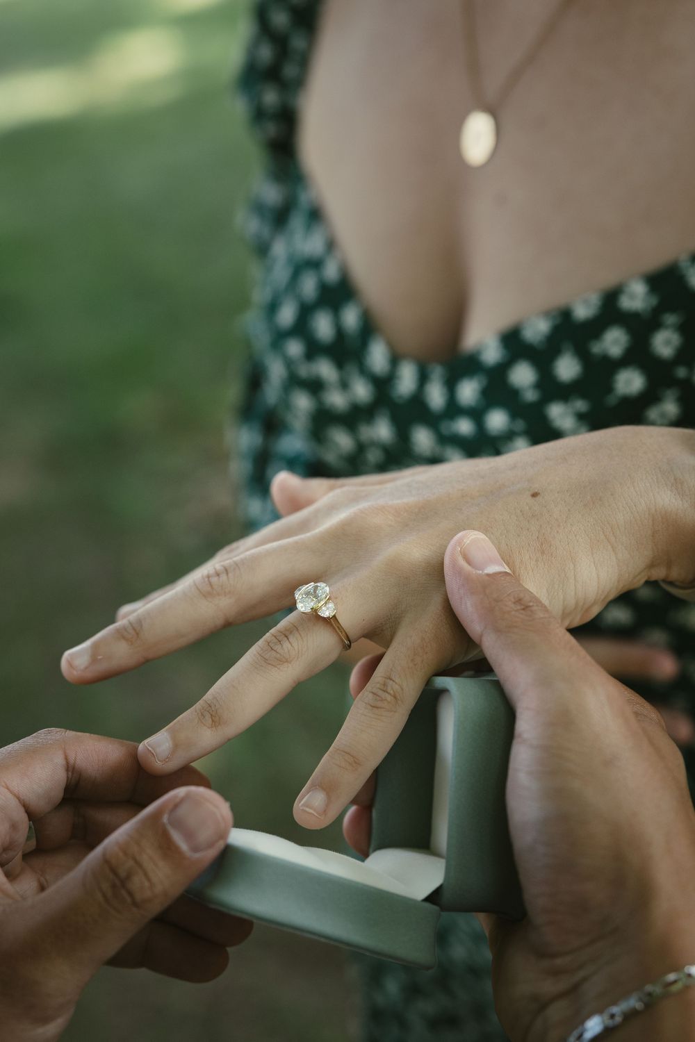 Close-up of a marriage proposal with a diamond solitaire ring being placed on a woman's finger outdoors.