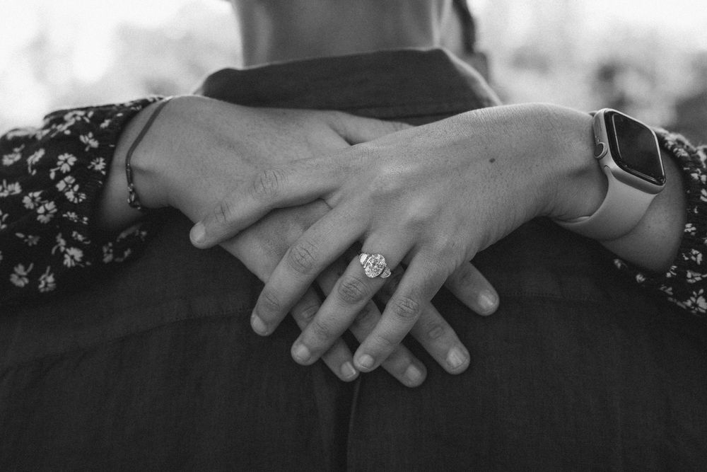 Black and white photo of couple embracing, woman wearing diamond engagement ring and smartwatch.
