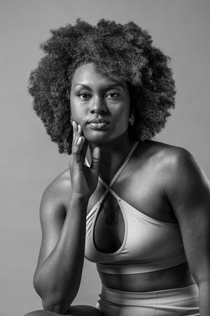 Black and white portrait of a woman with natural afro hair wearing a crop top, posing with hand on chin.