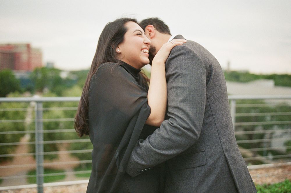 A couple shares a romantic embrace outdoors, with the woman smiling joyfully as the man kisses her cheek.