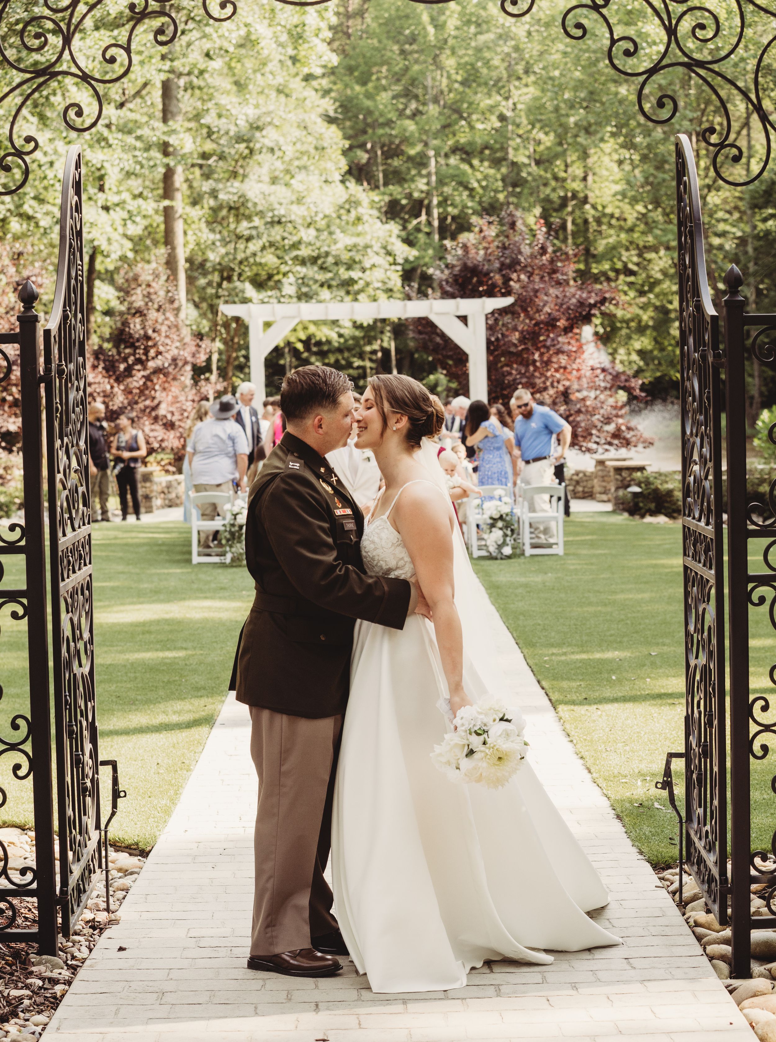 Bride and groom share a first kiss under ornate iron garden gates at an outdoor wedding ceremony.