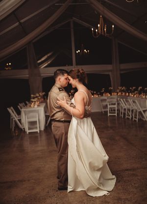 Bride and groom share an intimate first dance in a dimly lit elegant tent venue with candle-lit reception tables behind them.