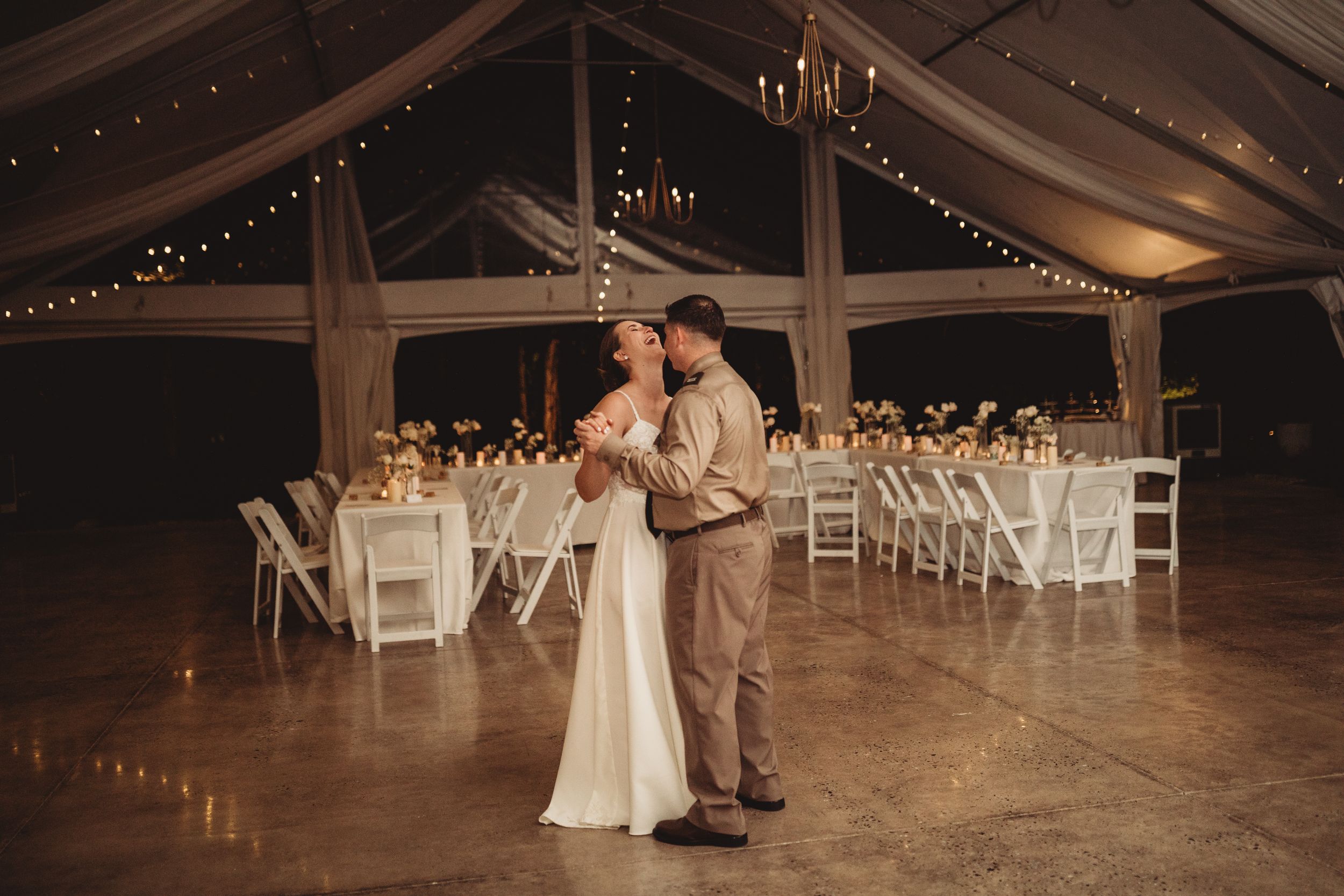 Bride and groom share first dance in elegant tent wedding venue with fairy lights and white floral centerpieces.