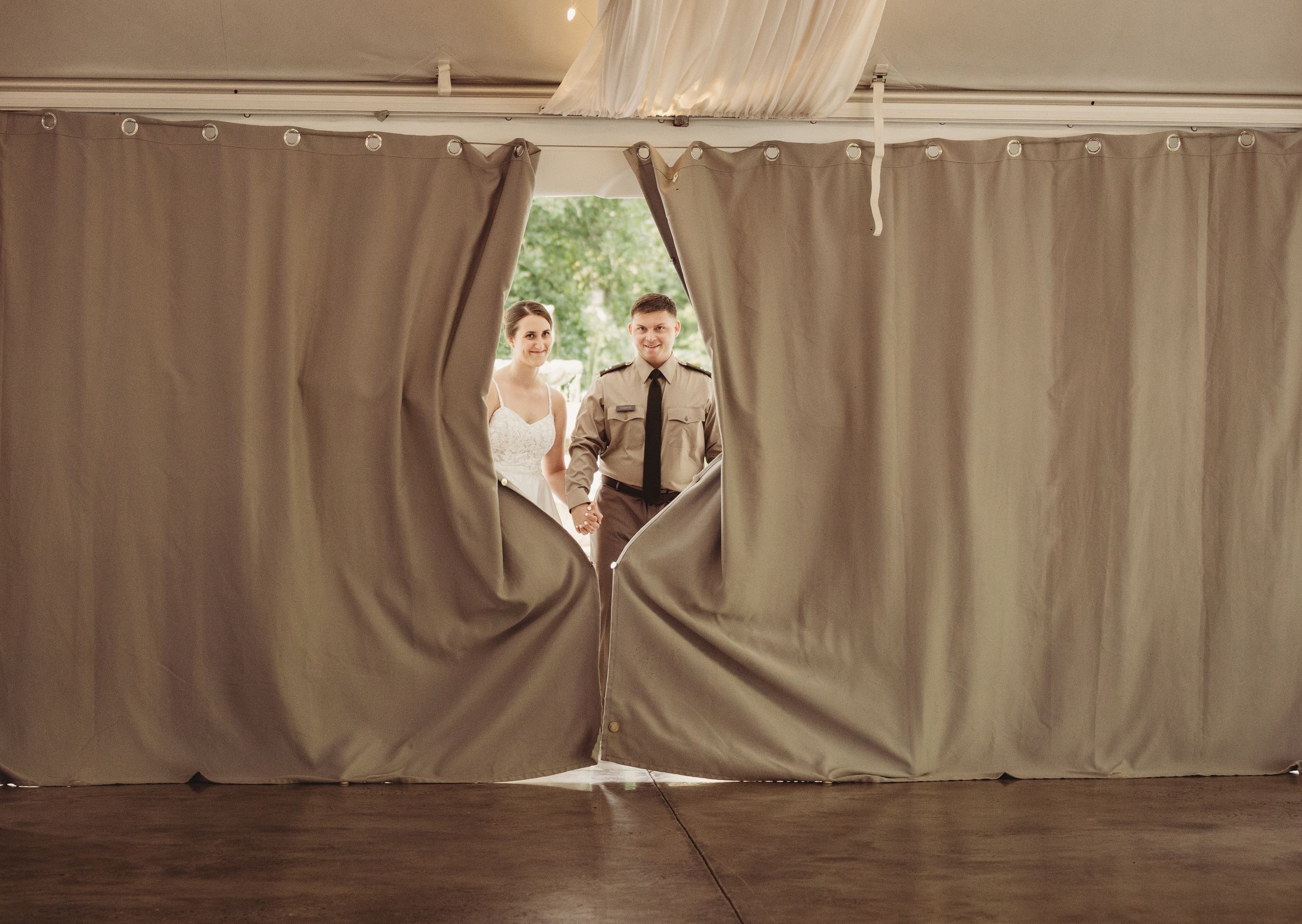 Bride and groom smiling as they part gray curtains to make a grand entrance at their wedding reception.