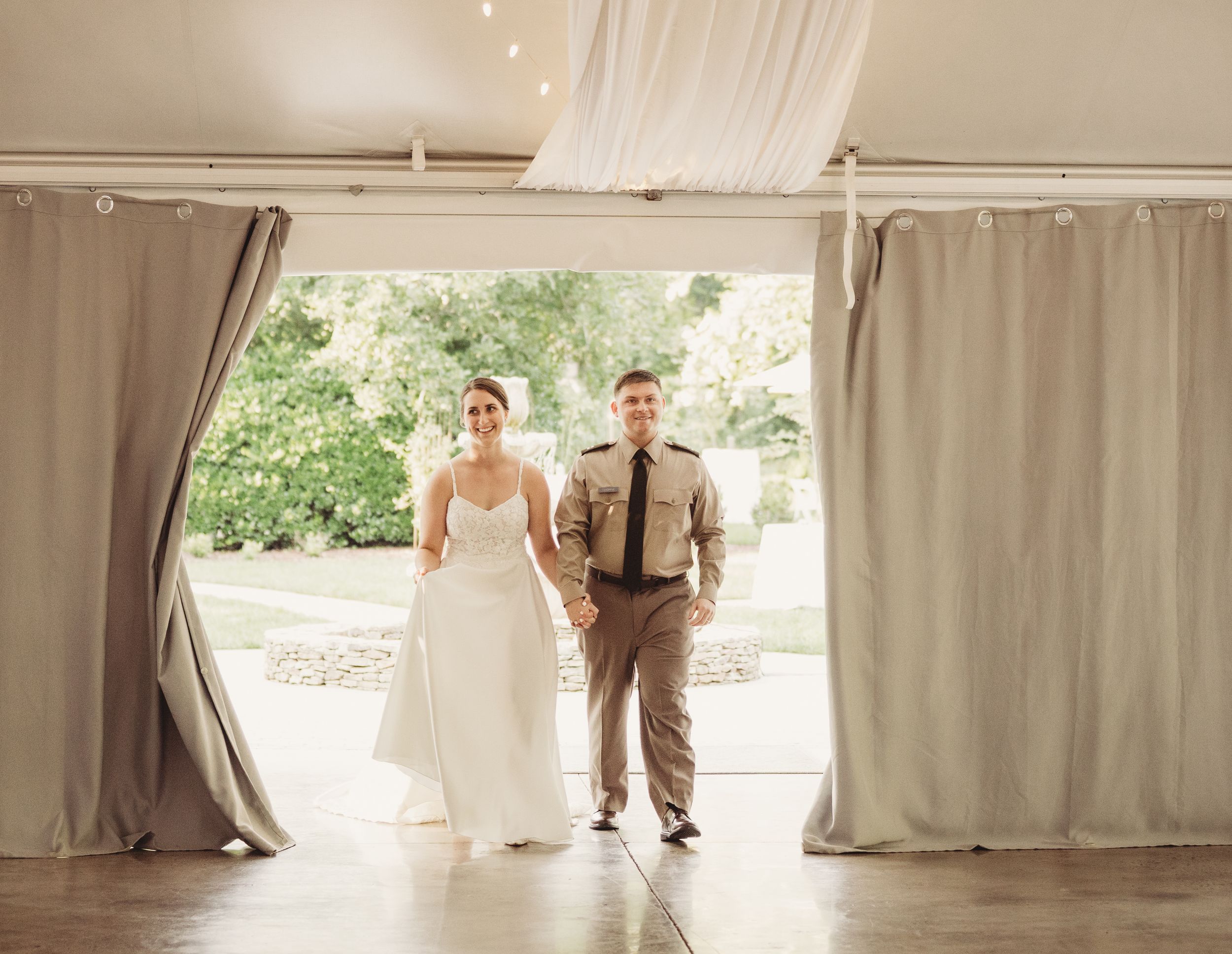 Bride and groom walking hand in hand through draped curtain entrance at elegant outdoor wedding venue.