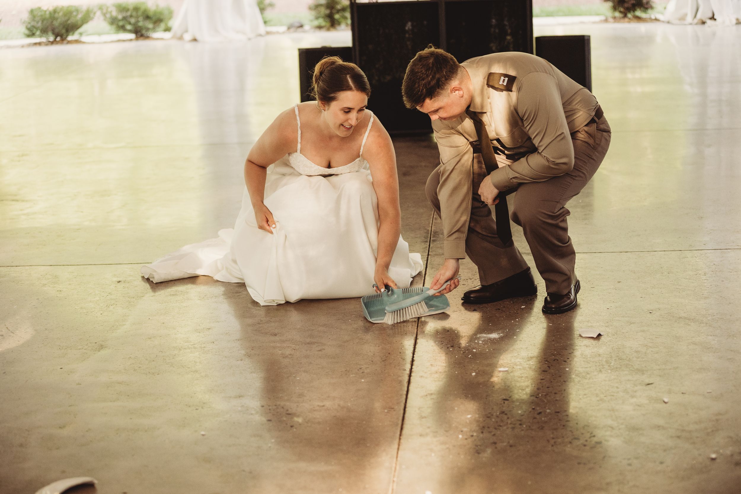 Bride and groom crouching on concrete floor at wedding reception venue, examining something together.
