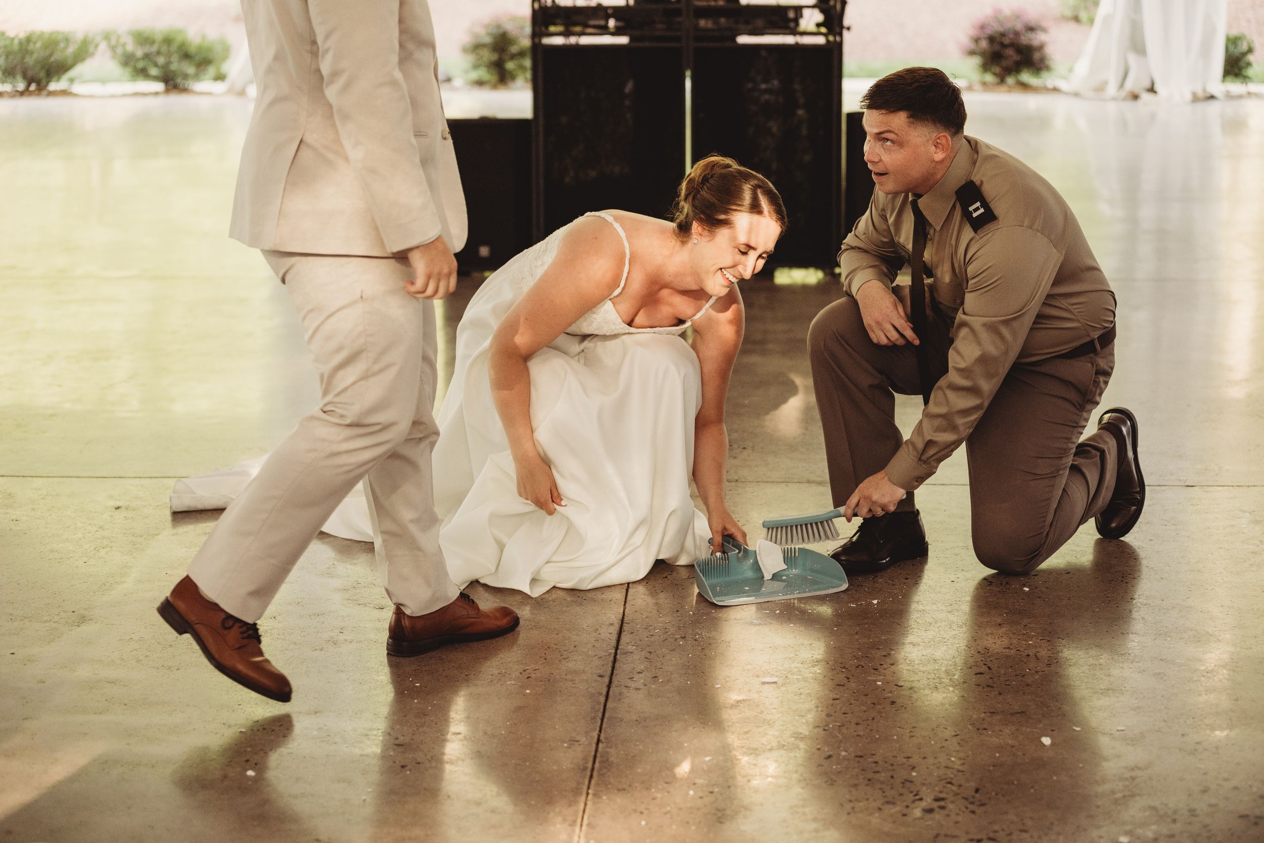 Bride in white dress and groom in military uniform pick up dropped item on dance floor at wedding reception.