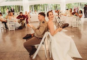 Bride and groom laugh during wedding reception game at elegant outdoor tent venue with guests seated at tables.
