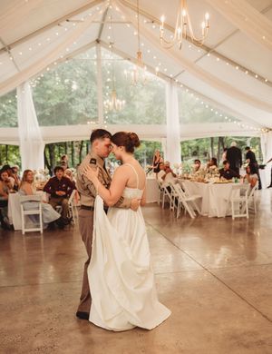 Bride and groom share first dance under elegant tent with string lights and chandeliers at outdoor wedding reception.