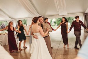 Bride and groom share first dance surrounded by wedding guests in burgundy attire under a white tent.