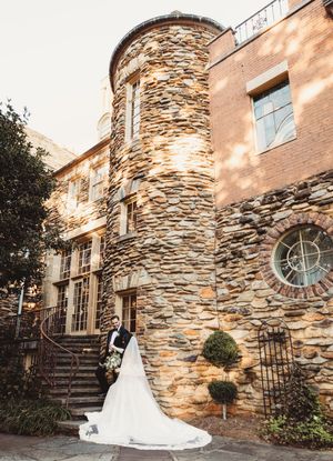 Bride and groom pose before a stone turret and brick building on their wedding day.