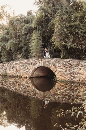 Wedding couple kisses atop a picturesque stone arch bridge reflected in calm water below.