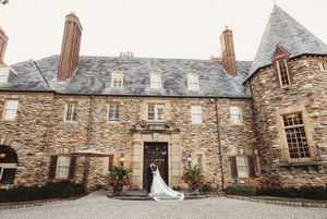 Bride and groom pose before grand stone castle wedding venue with cobblestone courtyard.
