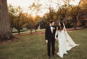 Bride and groom walk hand in hand through a sunlit park at golden hour in a romantic wedding portrait.