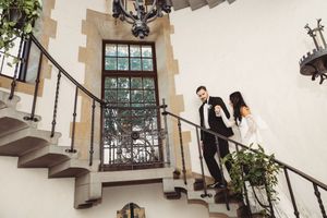 Bride and groom descend an elegant wrought iron staircase inside a grand castle wedding venue.