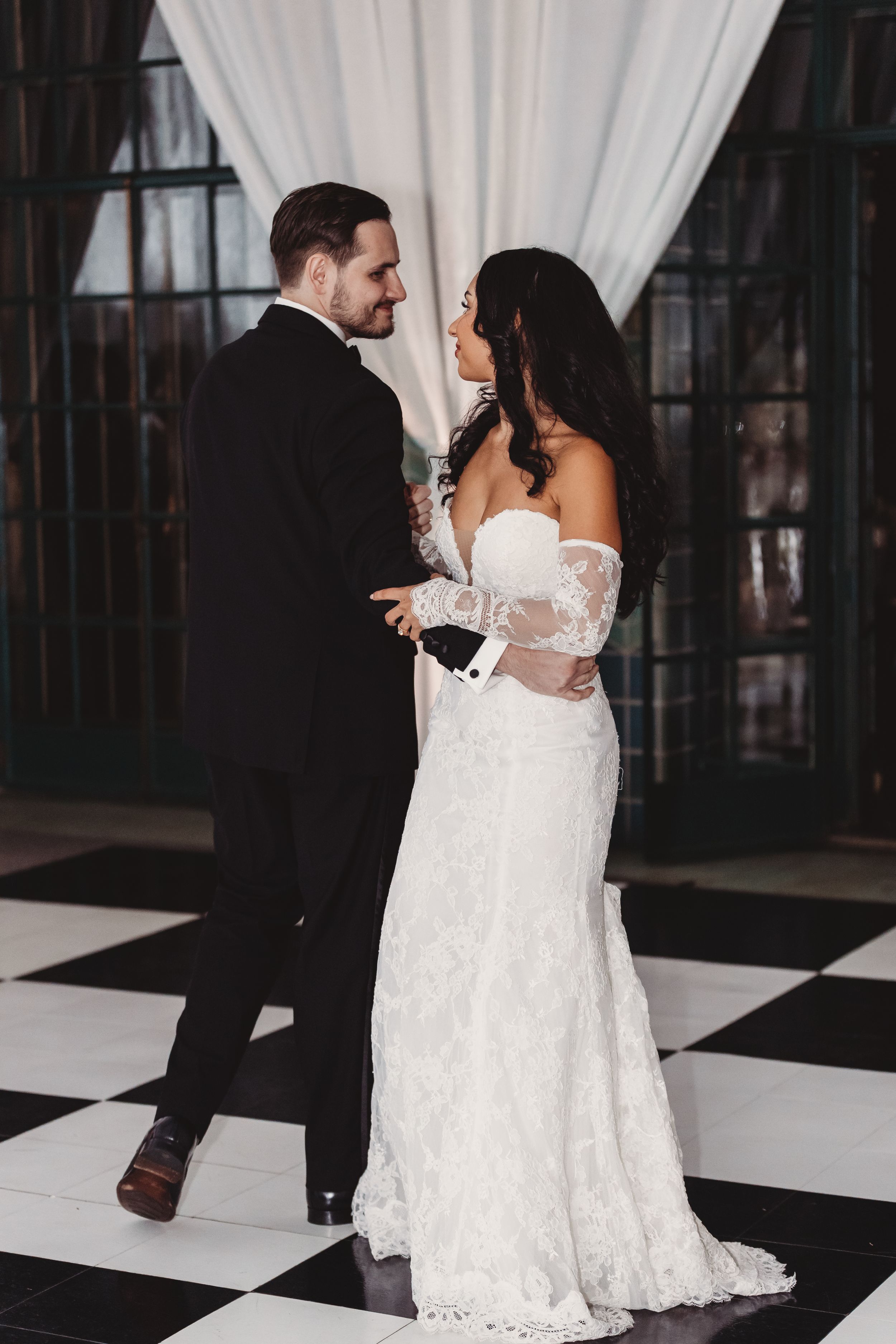 Bride and groom share an intimate moment on a black and white checkered dance floor during their elegant wedding reception.