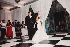 Bride and groom share first dance on black and white checkered floor at elegant wedding reception.