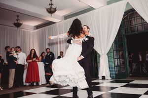 Groom lifts bride during energetic first dance on classic black and white checkered dance floor at wedding reception.