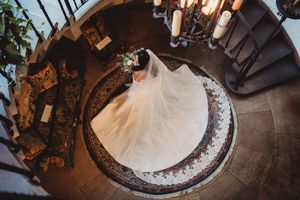 Aerial view of a bride in a stunning white ball gown with veil on a spiral staircase landing.