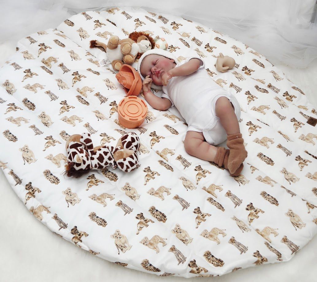 Baby lying on a round white play mat with safari animal print, surrounded by soft toys.