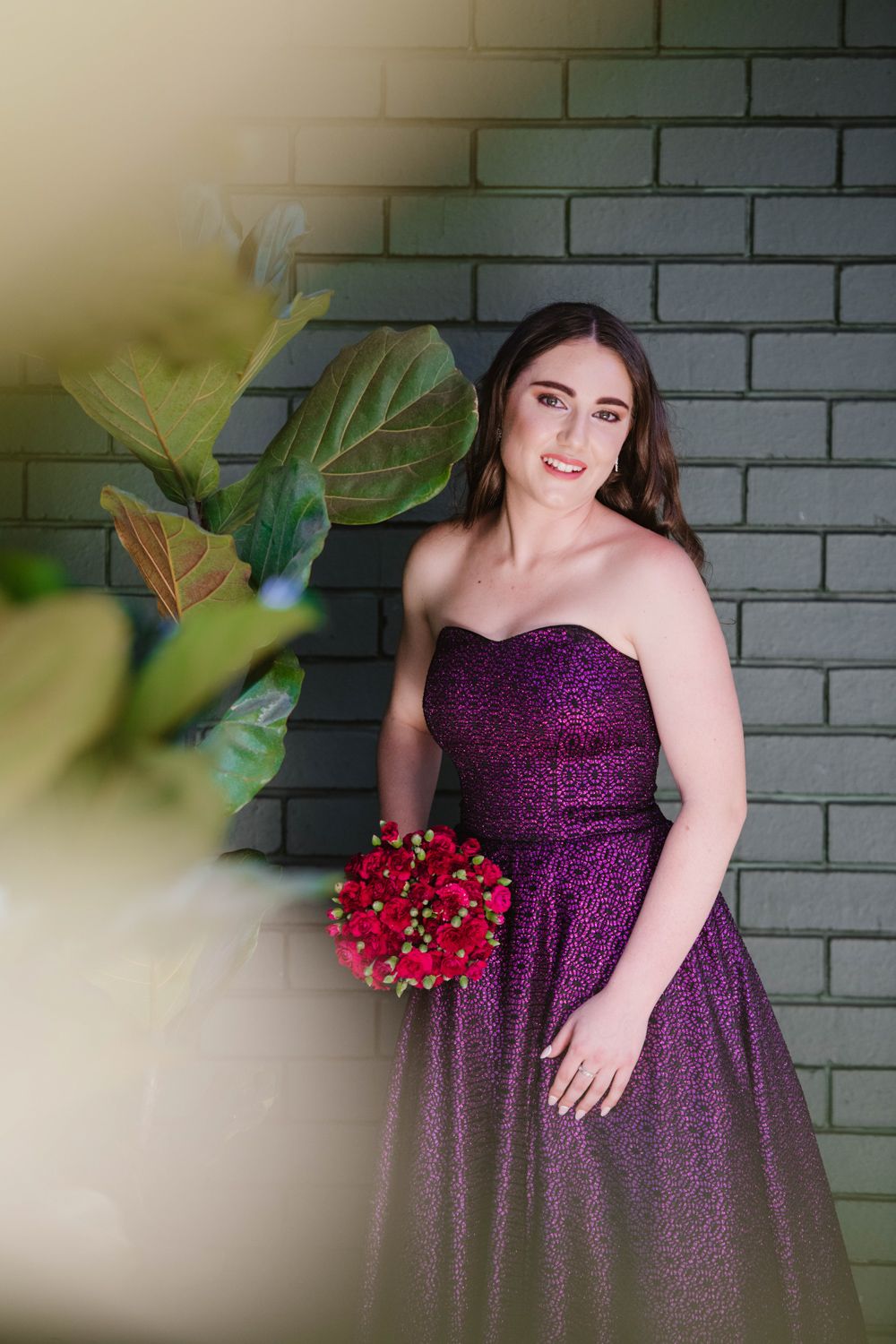 Matric dance learner posing in a stunning purple evening gown against a rustic brick wall for her Matriekafskeid.