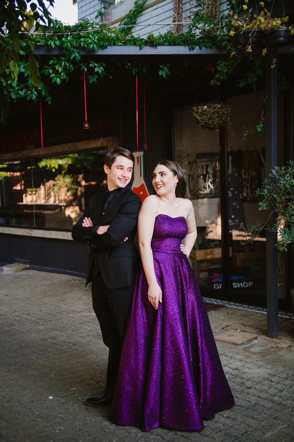 Couple posing on a walkway with a green ivy-covered wall background.