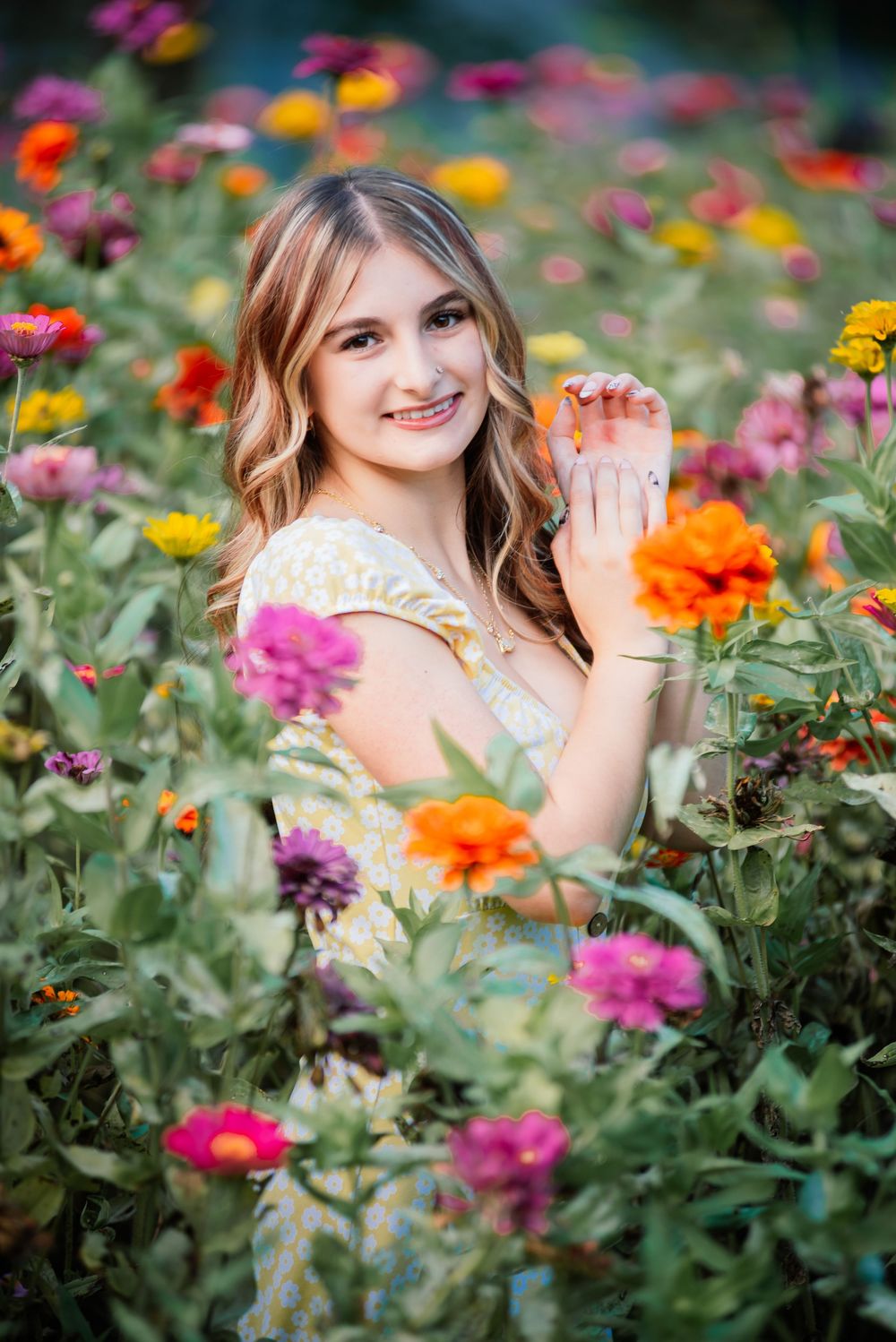 Young woman smiling in a vibrant flower field filled with colorful zinnias in pink, orange, and yellow.