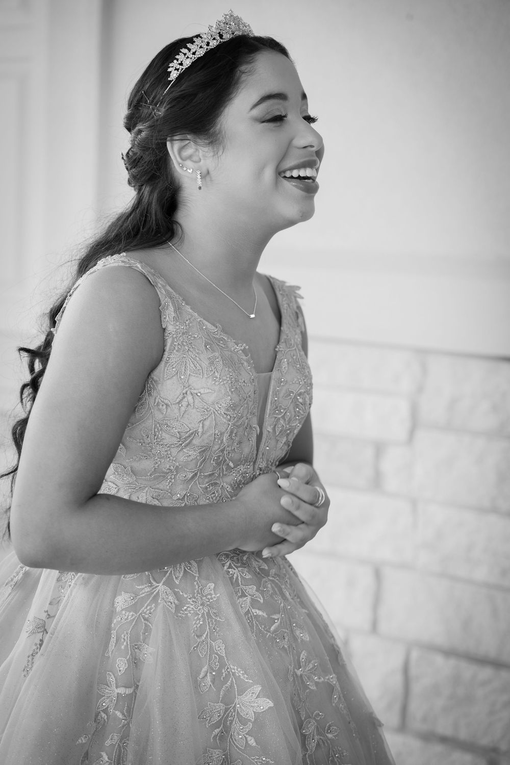 Young girl in embroidered ball gown and tiara laughing joyfully at a quinceañera celebration, black and white photo.