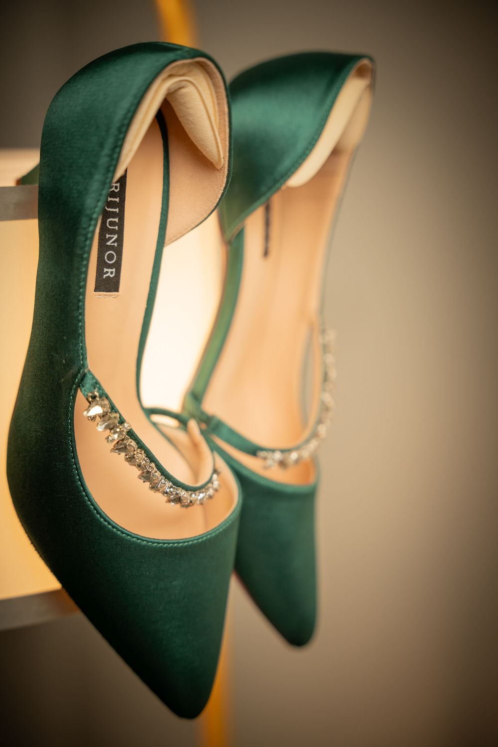 Elegant green satin pointed-toe heels with crystal embellishments displayed on a shelf.