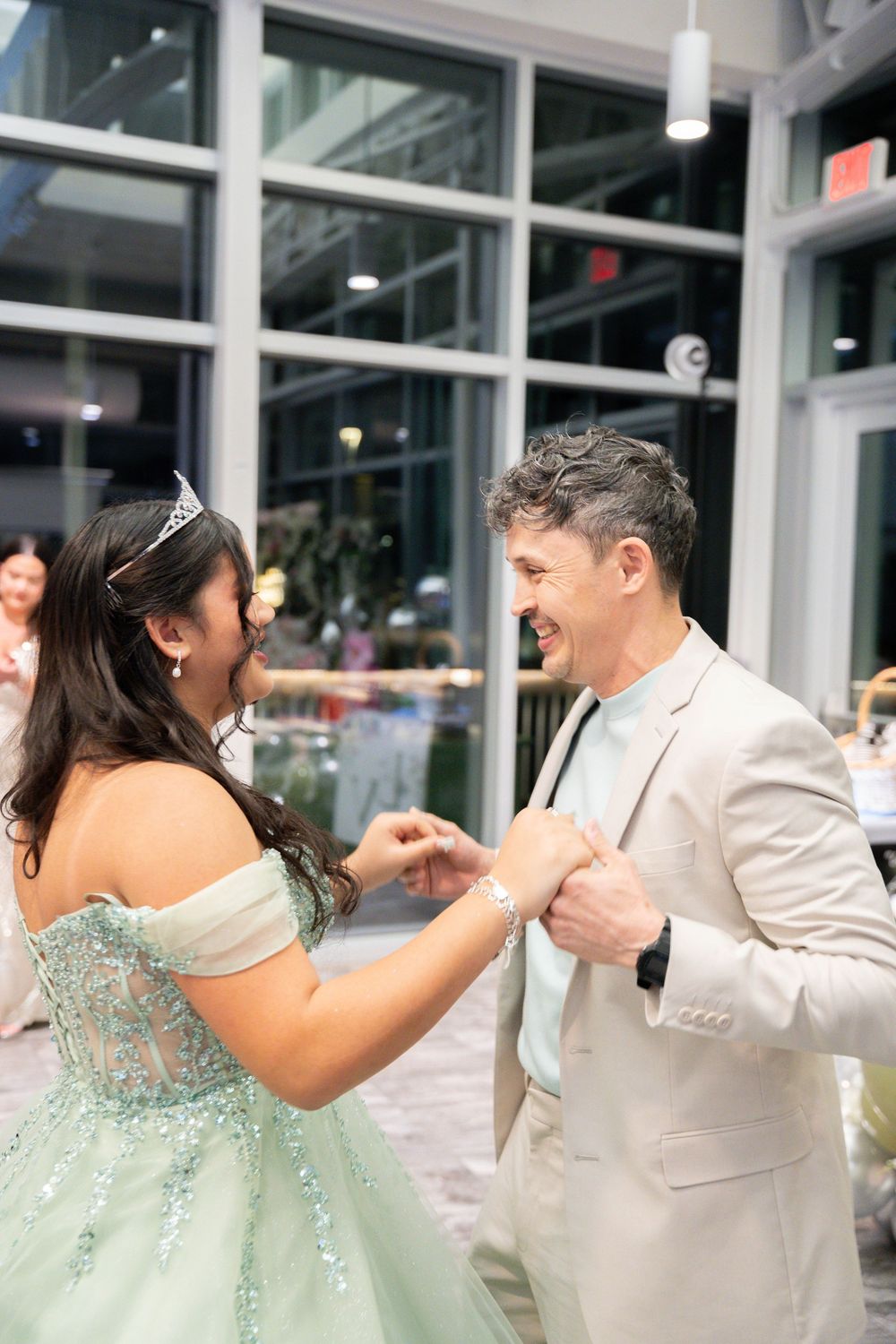 A young woman in a mint green quinceañera gown dances with a man in a beige suit at an elegant celebration.