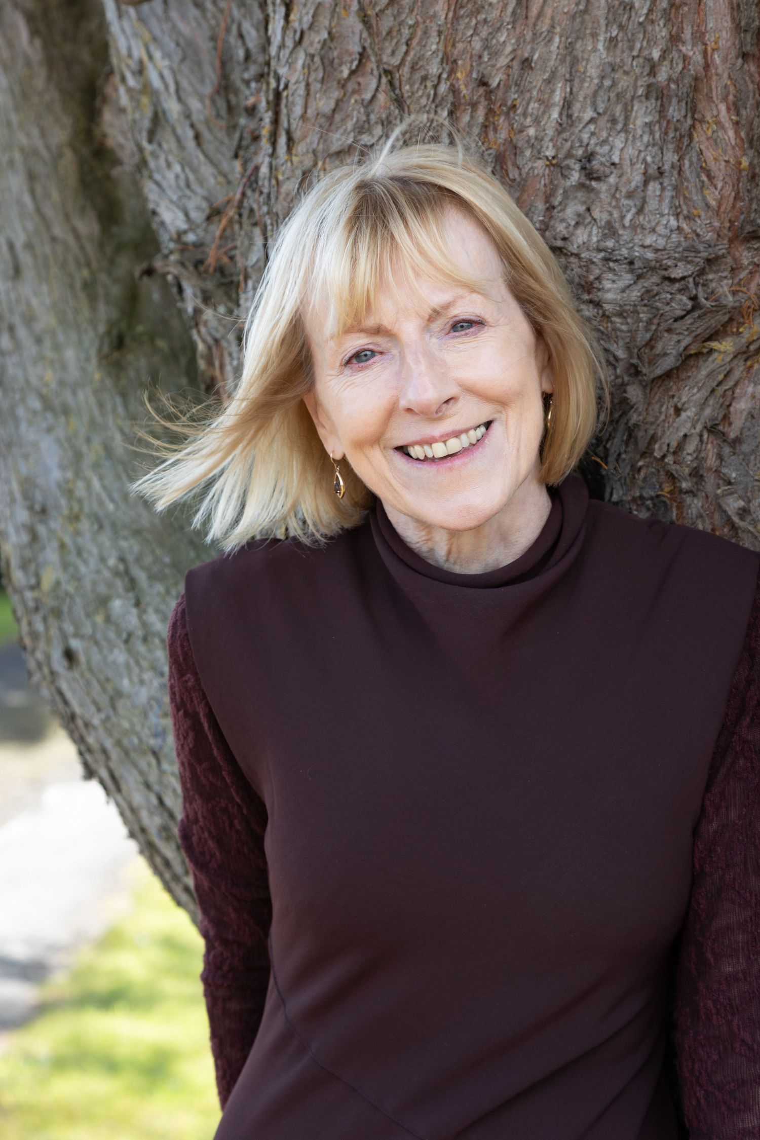 Headshot type portrait of a woman standing against a large tree truck.