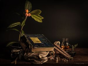 Vintage still life with antique books, whiskey glass, cigar, ink bottles, and a loquat branch on a wooden table.